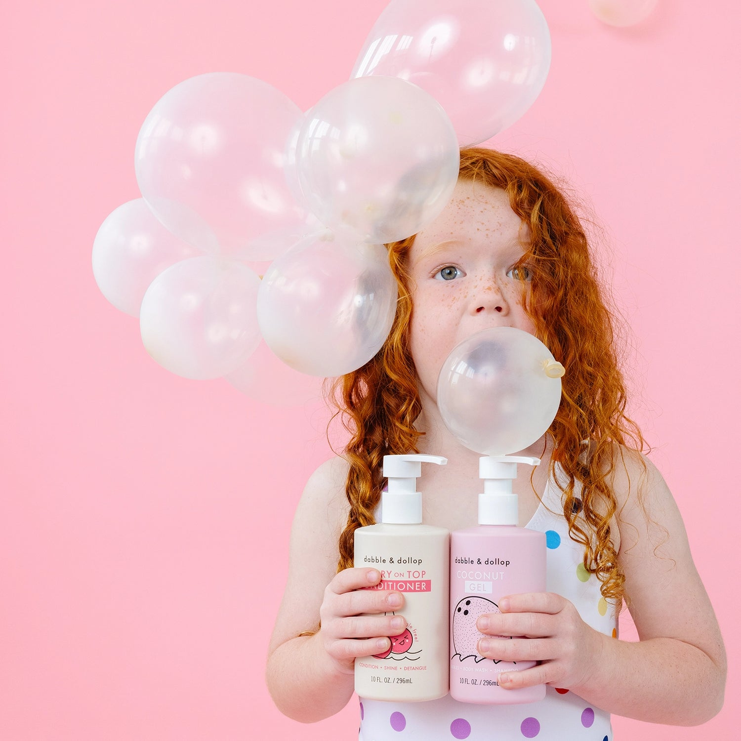 Girl blowing bubble holding two bottles of kids bath care products