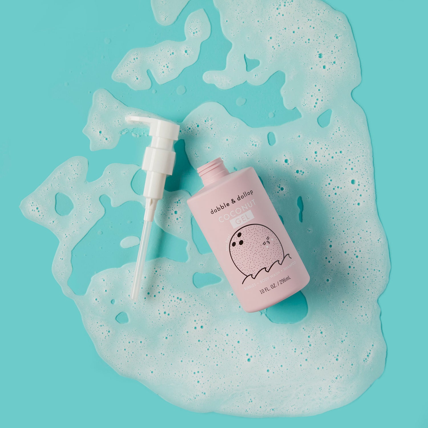 A pink bottle of Dabble & Dollop Coconut Bubble Bath, Body Wash & Shampoo with a white pump sits on a blue surface, surrounded by soapy bubbles.