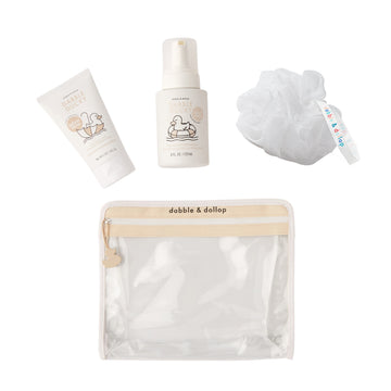 The Dabble & Dollop Infant Bundle is a limited edition set featuring EWG Verified, fragrance-free baby wash in a white tube and pump bottle, plus a bath pouf, all in a clear beige-trimmed pouch with playful branding and illustrations.
