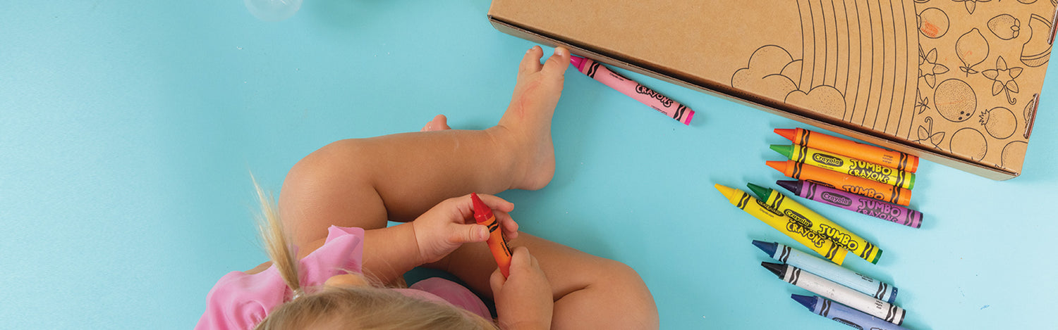 Little child coloring with crayons on a Dabble & Dollop Rainbow of Bubbles box