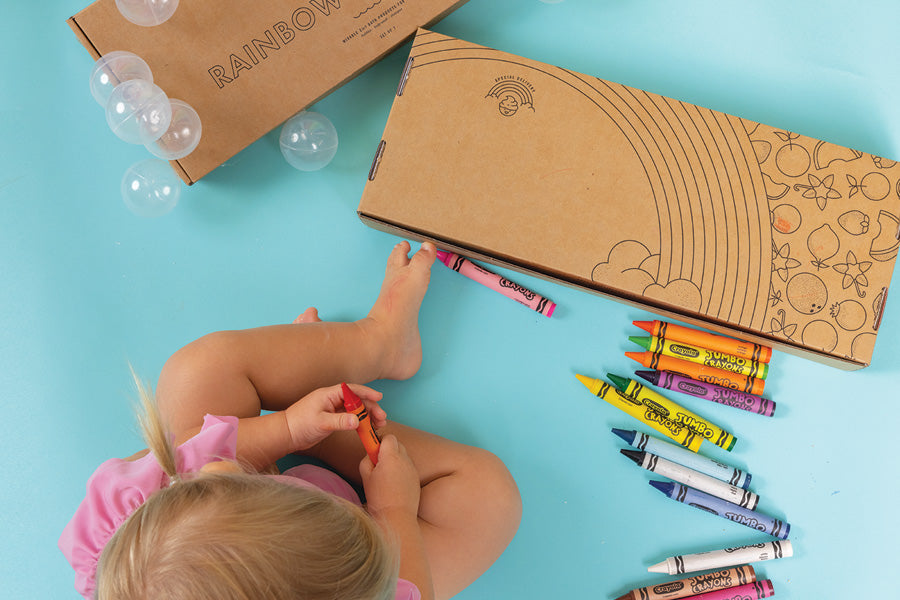 Little child coloring with crayons on a Dabble & Dollop Rainbow of Bubbles box