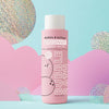 A bottle of Dabble & Dollop Coconut Bubble Bath, adorned with playful coconut illustrations on the label, sits on a pastel backdrop accented by shiny iridescent circles and pink cloud shapes. This gentle, hypoallergenic, and tear-free Coconut Bubble Bath brings fun to bath time for little ones.