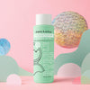 A green bottle of Dabble & Dollop Honeydew Bubble Bath is displayed among pastel shapes on a pink background, accented by shiny, iridescent decorative circles. Specially designed for kids, its tear-free formula is gentle on sensitive skin.