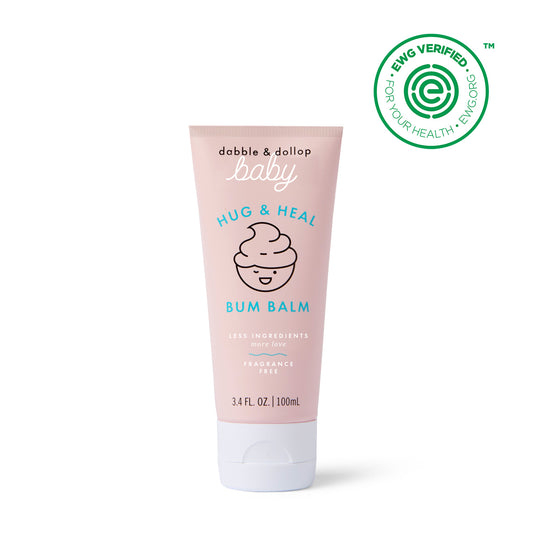 A pink tube of Dabble & Dollop Hug & Heal™ Bum Balm (3.4 fl oz/100 ml) features a smiling swirl and an EWG Verified™ seal, offering gentle diaper care for babies.