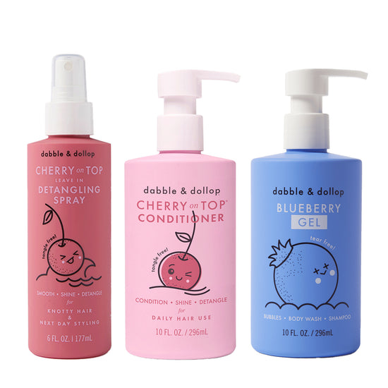Three colorful bottles of Dabble & Dollop Detangler and Conditioner feature playful fruit designs and pump or spray tops, including pink detangling spray, pink conditioner, and blue gel.