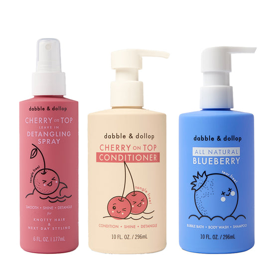 Three bottles of dabble & dollop: Detangler and Conditioner with cherry (pink spray), Conditioner with cherry (beige), and All Natural Blueberry Bubble Bath (blue), each featuring cute fruit illustrations.
