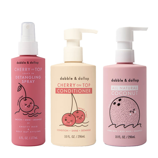 Three Dabble & Dollop bottles: pink Cherry Detangler, pale pink Cherry Conditioner, and light pink Coconut Bubble Bath, each with cute fruit characters on the packaging.