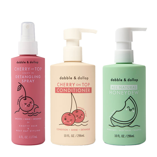 Three Dabble & Dollop bottles: pink Detangler and Conditioner with pump, cream Conditioner, and green All Natural Honeydew Body Wash, each featuring cute fruit illustrations and convenient pump or spray tops.
