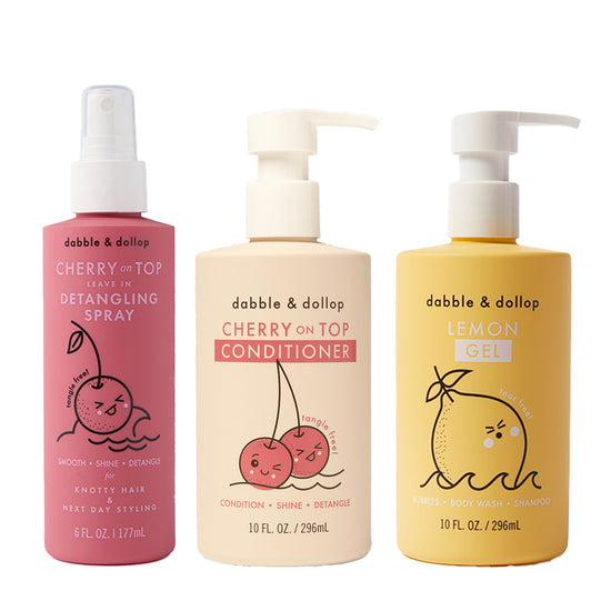 Three bottles of Dabble & Dollop hair products: Detangler with pump, Conditioner with cherry graphics and pump, and Lemon Gel Shampoo with lemon graphic and pump top.