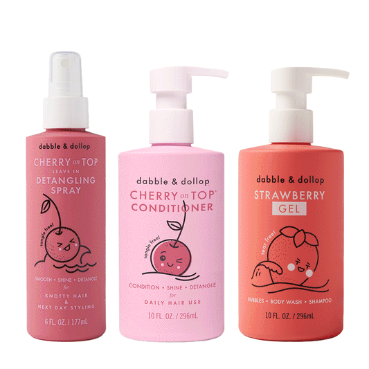 The Dabble & Dollop Bath to Brush Bundle features three colorful bottles—pink detangling spray, light pink conditioner, and red strawberry gel—each with playful fruit illustrations and convenient pump or spray tops.