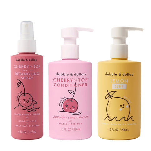 Three bottles of Dabble & Dollop kids' products: "Cherry on Top" Detangler and Conditioner (both pink), and "Lemon Gel" Body Wash (yellow), each featuring playful fruit illustrations.