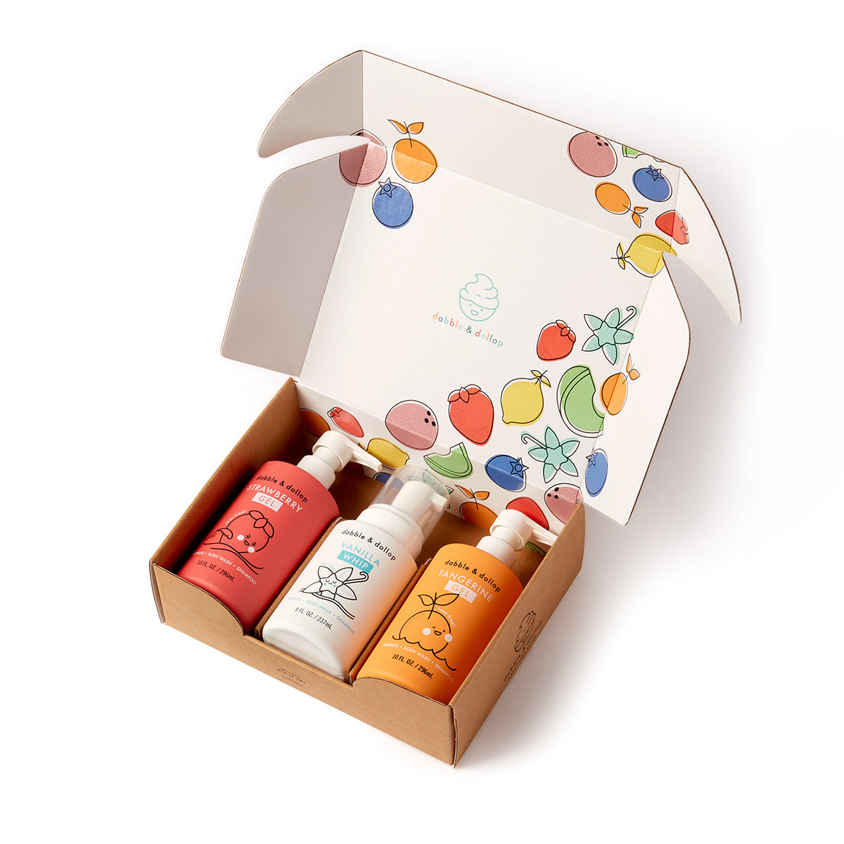 An open cardboard box with colorful fruit illustrations contains three bottles of Dabble & Dollop’s Build Your Own Bath Bundle—one red, one white, and one orange—each with simple fruit graphics and pump dispensers.