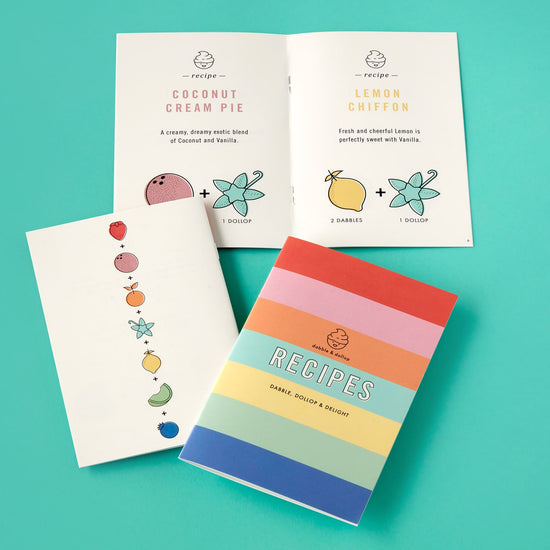 Three Dabble & Dollop recipe booklets on a teal background highlight creativity and fun. One open booklet features recipes for Coconut Cream Pie and Lemon Chiffon with graphics, while the others display pastel fruit illustrations, rainbow stripes, and the word Recipes.