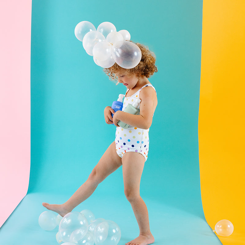 Girl holding bath products with balloon bubbles on head