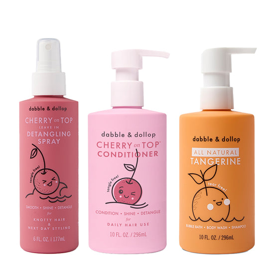 Three colorful Dabble & Dollop bottles: a pink Detangler, a lighter pink Conditioner, and an orange Tangerine Bubble Bath—each featuring cute fruit illustrations on the label.