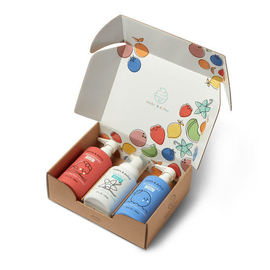 The Dabble & Dollop Americana Bath Bundle includes three bubble baths in red, white, and blue packaging, arranged in an open box decorated with colorful fruit illustrations on the inside lid.