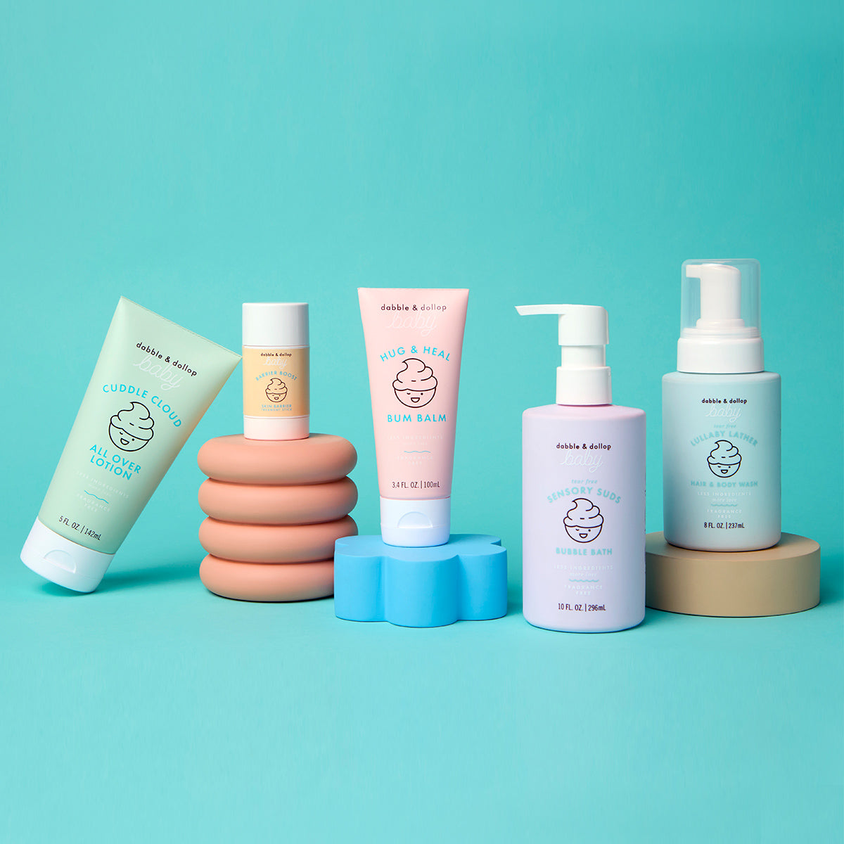 Five pastel-colored Dabble & Dollop baby skincare products, including the gentle Hug & Heal™ Bum Balm with zinc oxide, stand on decorative pedestals against a turquoise background—perfect for caring for your baby's sensitive skin.