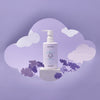 A bottle of Dabble & Dollop Sensory Suds™ Bubble Bath with a pump rests on a white block with cloud and flower cutouts against a purple background, creating a dreamy, whimsical scene.