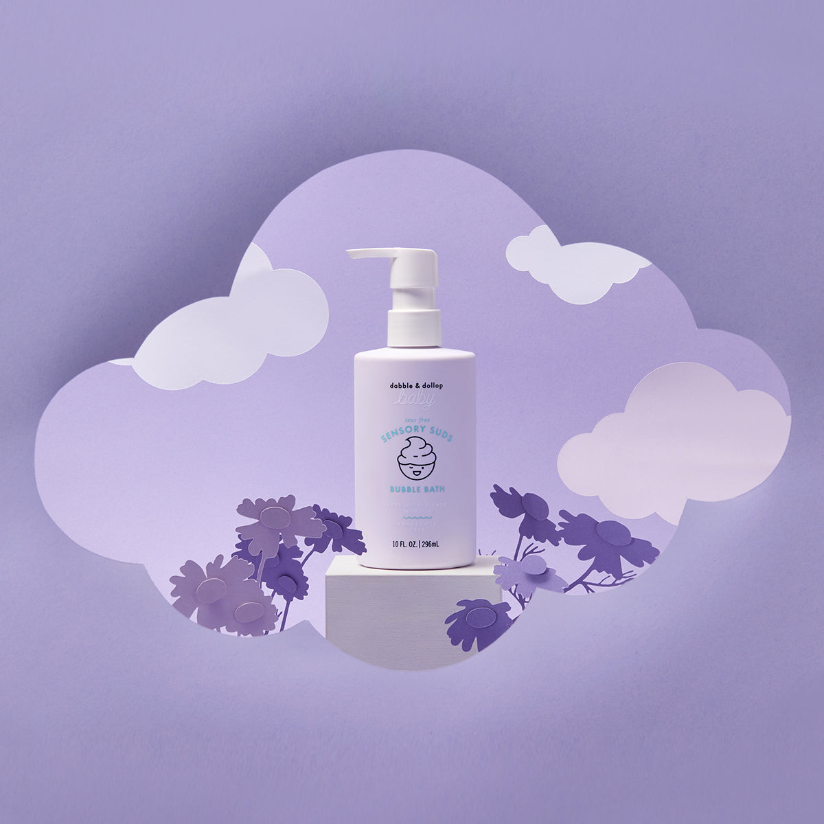 A bottle of Dabble & Dollop Sensory Suds™ Bubble Bath with a pump rests on a white block with cloud and flower cutouts against a purple background, creating a dreamy, whimsical scene.