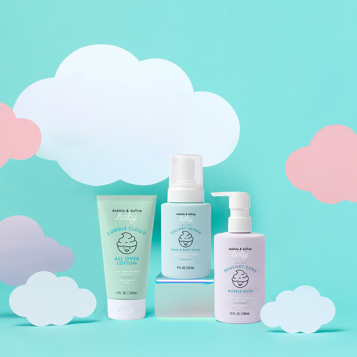 Three pastel-colored bottles of Dabble & Dollop’s Baby Bath to Bed Gift Set are displayed against a light blue background with white and pink paper clouds. This set features lotion, hair & body wash, and bubble bath—all specially formulated for sensitive baby skin.