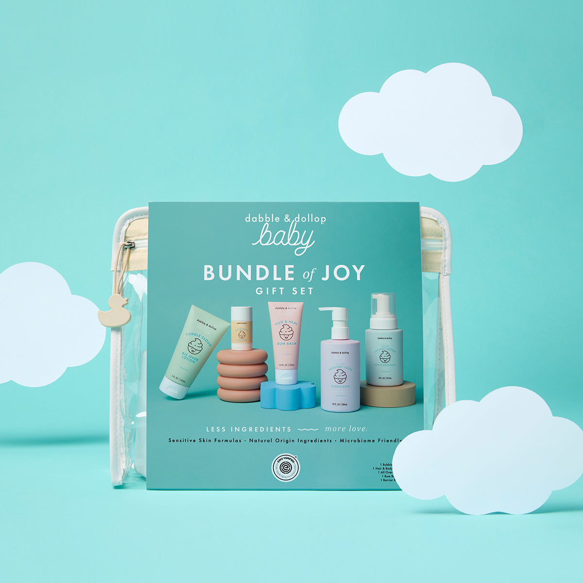 The Bundle of Joy Gift Set by Dabble & Dollop is shown in a clear pouch against a blue background with white paper clouds and features pastel-colored baby skincare products.