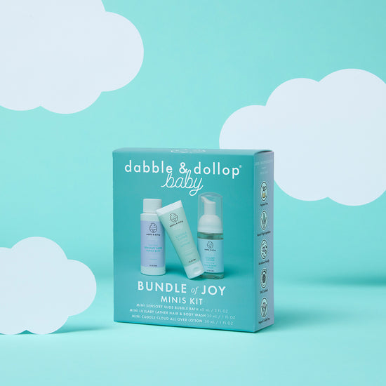 A teal box labeled "Dabble & Dollop Bundle of Joy Minis Kit" displays three travel-size baby care products on a turquoise background with white cloud illustrations.