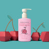 A pink bottle of Dabble & Dollop Cherry on Top® Hair Conditioner with a smiling cherry illustration sits among three paper cherries on a teal background. This cherry-scented conditioner keeps kids’ haircare fun and gentle.
