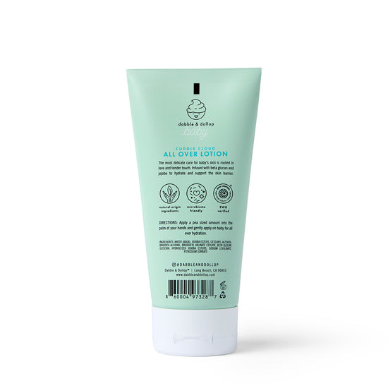 A mint green tube of Dabble & Dollop Cuddle Cloud™ All Over Lotion stands upright, displaying the back label with product details, usage directions, ingredients, and icons for natural ingredients and sensitive skin suitability.