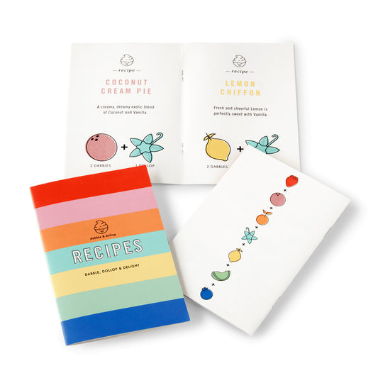 Three vibrant booklets are shown: one closed with a rainbow-striped RECIPES cover, and two open with coconut and lemon dessert recipes made with clean ingredients—perfect companions to the Dabble & Dollop Original Bubble Bath Bundle.