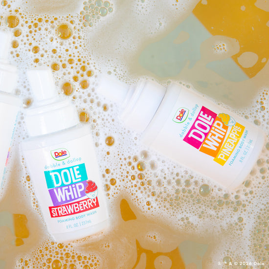 Two bottles of Dabble & Dollop Dole Whip® Pineapple Foaming Body Wash on bubbly, colorful water show off playful labels and natural origin fragrance, creating a fresh and fun scene.