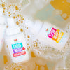 Two bottles of Dabble & Dollop Dole Whip® Pineapple Foaming Body Wash on bubbly, colorful water show off playful labels and natural origin fragrance, creating a fresh and fun scene.