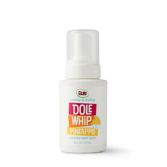 An 8 fl. oz. white bottle of Dabble & Dollop Dole Whip® Pineapple Foaming Body Wash with a pump, featuring yellow and pink text and a whipped dessert illustration. Hypoallergenic formula included.