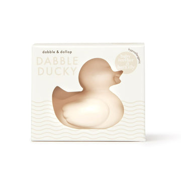The packaging features a cream-colored Ducky Bath Toy & Teether by Dabble & Dollop. Made in the USA, its a hypoallergenic, phthalate-free toy. The minimalist box with wavy lines ensures safe and fun bath time adventures.