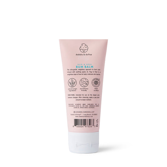 A pink tube of Dabble & Dollop Hug & Heal™ Bum Balm diaper cream with zinc oxide and a white cap, showing product info, usage directions, and natural ingredient icons for baby's sensitive skin. The back label is visible.