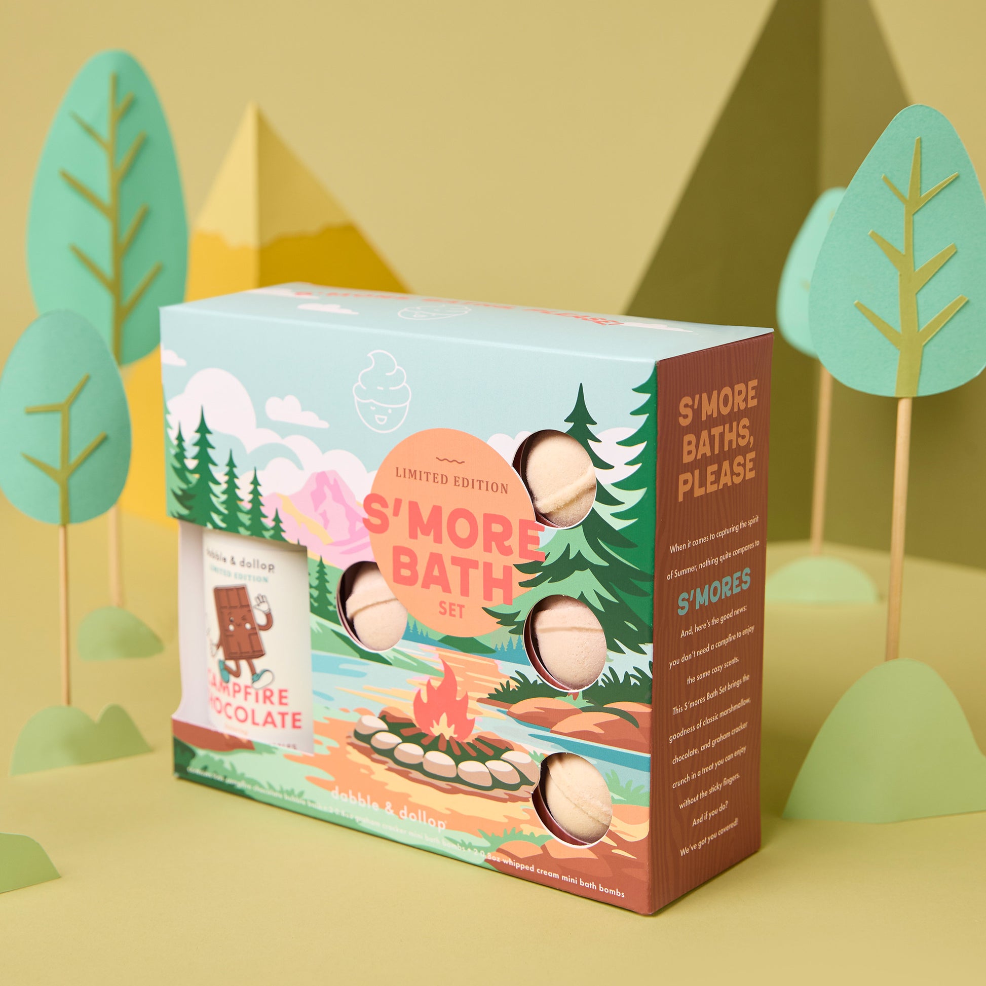 Dabble & Dollop's S'more Bath Set is a limited edition kids box featuring six round bath bombs and Campfire Chocolate, with campfire, trees, and mountains illustrated on a pastel woodland background.