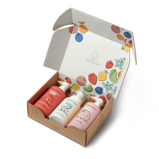 A cardboard gift box with colorful fruit illustrations inside the lid, containing three Sweetheart Bath Bundle bottles by Dabble & Dollop, featuring playful, minimal fruit and animal designs on their plant-based bath product labels.