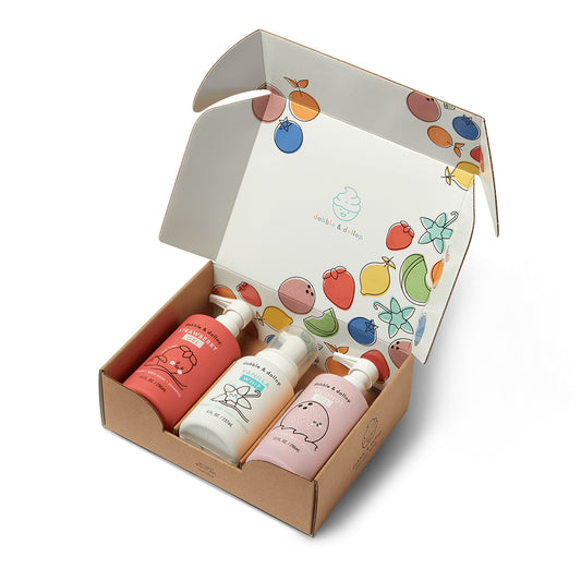 A cardboard gift box with colorful fruit illustrations inside the lid, containing three Sweetheart Bath Bundle bottles by Dabble & Dollop, featuring playful, minimal fruit and animal designs on their plant-based bath product labels.