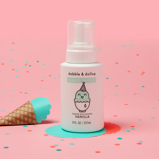 A Dabble & Dollop Vanilla Hand Wash bottle, featuring a playful ice cream design, is placed on a pink background with colorful confetti and a toy ice cream cone nearby.