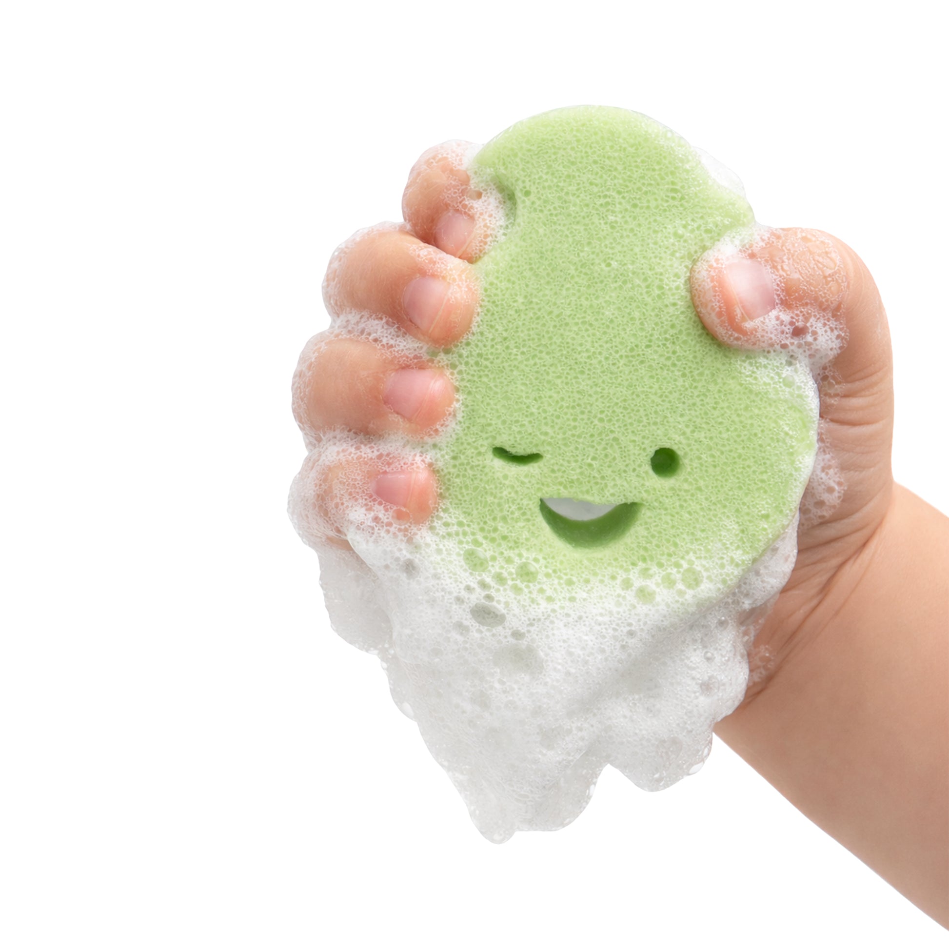 A hand squeezes Dabble & Dollop's Sponge Pop™ Sponge with Built-In Body Wash, a green biodegradable sponge with a winking smile, covered in foamy bubbles against a white background.